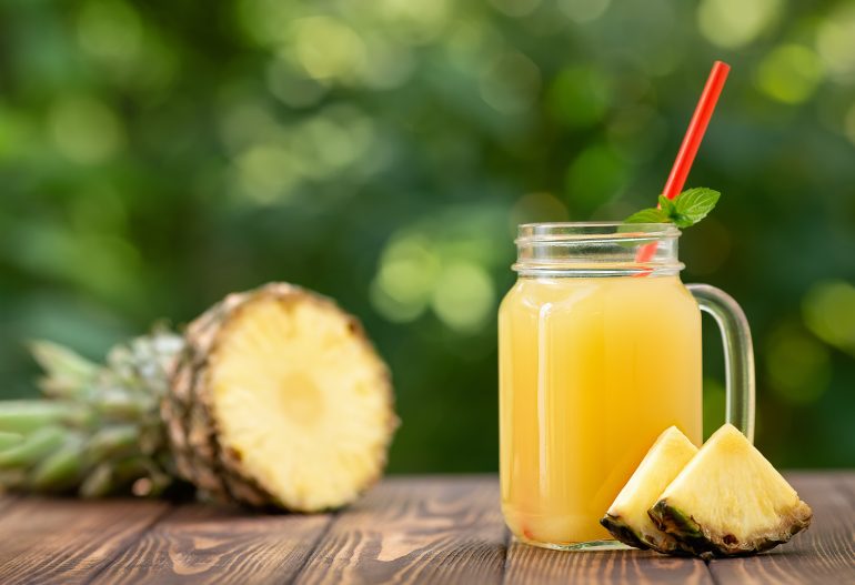 fresh pineapple juice in glass mason jar and ripe fruit on wooden table outdoors. Summer refreshing drink
